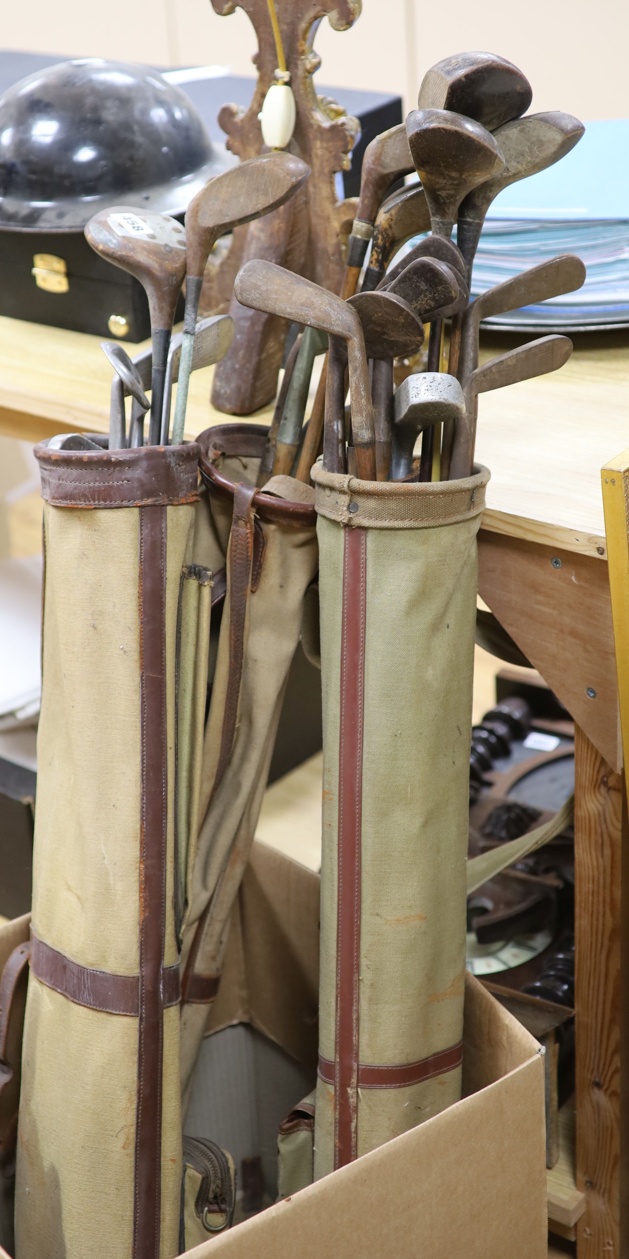 A collection of pre-war golfing irons and woods, contained within three canvas golf bags